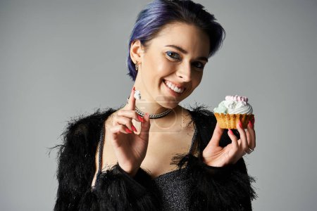 Téléchargez les photos : A young woman with blue hair holding a delicious cupcake in a studio setting, exuding a festive birthday vibe. - en image libre de droit