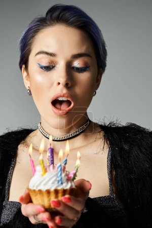 Foto de Stylish young woman holds a cupcake topped with lit candles. - Imagen libre de derechos