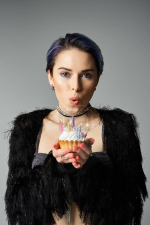 Téléchargez les photos : A pretty young woman with short dyed hair poses in stylish attire, holding a delicious cake in her hand. - en image libre de droit