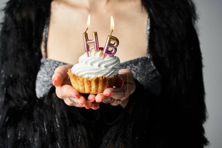 Téléchargez les photos : A stylish young woman with short dyed hair holding a cupcake with burning candles in a studio setting. - en image libre de droit