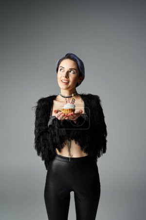 A stylish young woman in black attire holding a delicious cupcake with candles