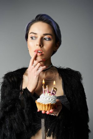 A young woman in stylish attire holds a cupcake with lit candles, a birthday girl ready to make a wish.