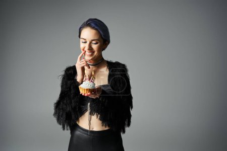 Foto de A young woman with stylish attire holding a cupcake in front of her face, adding a touch of sweetness to her birthday celebration. - Imagen libre de derechos