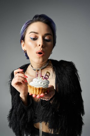 Young woman in fashionable attire holding a cupcake with a lit candle, showcasing a magical moment.