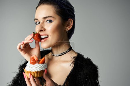 Foto de Young woman in black dress enjoying a cupcake with fresh strawberries - Imagen libre de derechos