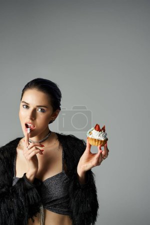 Téléchargez les photos : A stylish young woman with dyed hair poses with a cupcake, taking a bite from it. - en image libre de droit