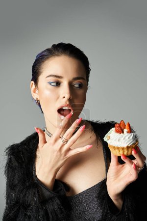 Young woman in black dress holding a cupcake.