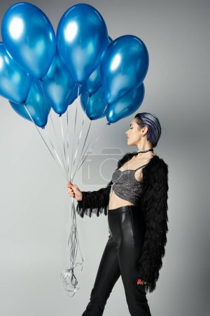 Photo for A stylish young woman with short dyed hair gracefully holds a bunch of vibrant blue balloons. - Royalty Free Image
