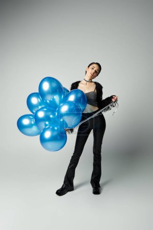 A vibrant young lady with chic style clutches a bunch of radiant blue balloons.