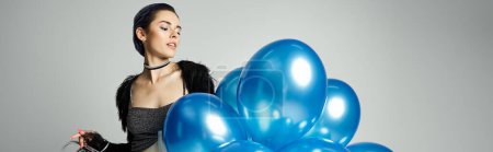Foto de A young birthday girl with stylish attire holding a bunch of blue balloons in a studio setting. - Imagen libre de derechos