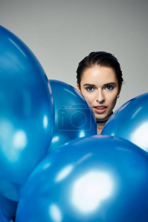 Young woman with short dyed hair holding a bunch of blue balloons. She radiates happiness.