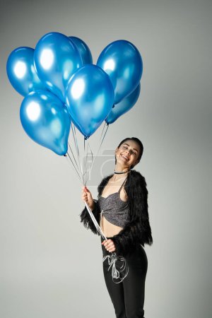 Foto de A stylish young woman with short dyed hair poses happily while holding a bunch of blue balloons. - Imagen libre de derechos