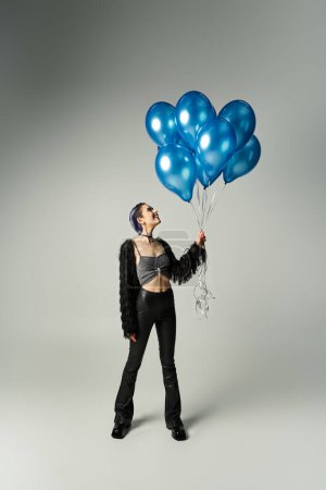 Foto de A vibrant woman with short dyed hair joyfully holds a bunch of blue balloons in a studio setting. - Imagen libre de derechos