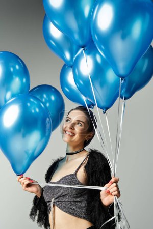 A young woman with colorful hair holding a bundle of blue balloons in a stylish studio.