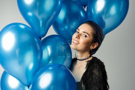 A stylish young woman with short dyed hair posing happily while holding a bunch of bright blue balloons.