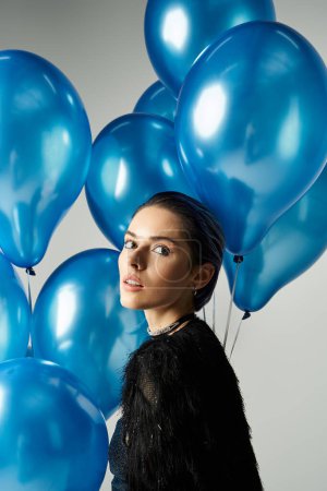 Young woman with dyed hair stands in front of a group of blue balloons, exuding elegance and style.