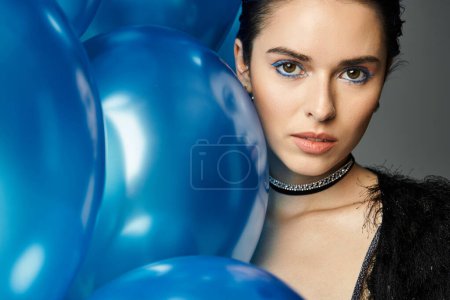 A young woman with striking blue eyes holds a group of vibrant balloons, radiating joy and celebration.