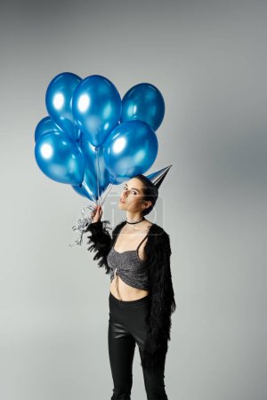 Téléchargez les photos : Short-haired young woman in chic attire joyfully holding a bunch of vibrant blue balloons in a studio setting. - en image libre de droit