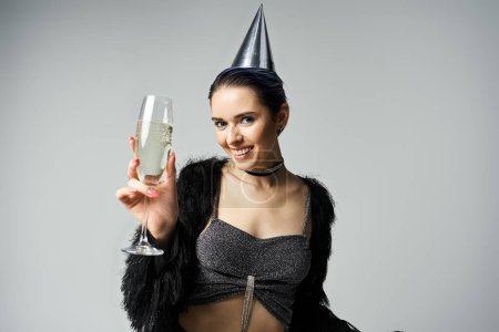 Téléchargez les photos : Young woman in fashionable outfit and party hat holds champagne glass for birthday celebration. - en image libre de droit