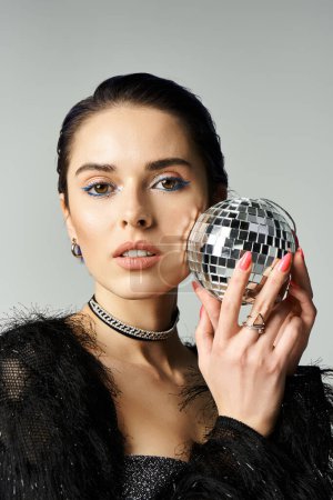 A stylish young woman in a black dress holding a sparkling disco ball in a captivating pose.