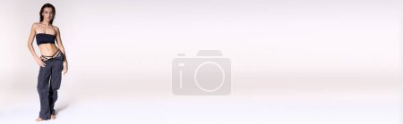 Photo for Stylish woman in black bikini top poses against white backdrop. - Royalty Free Image