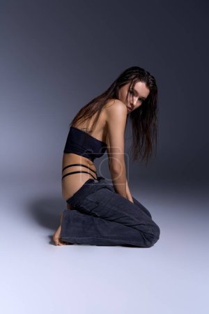 A stylish young woman sits on the ground with wet hair.