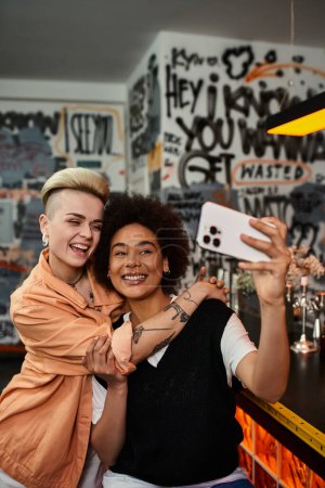 Zwei wunderschöne Lesben fangen einen Moment in einer schwach beleuchteten Bar ein, als sie zusammen ein Selfie machen.