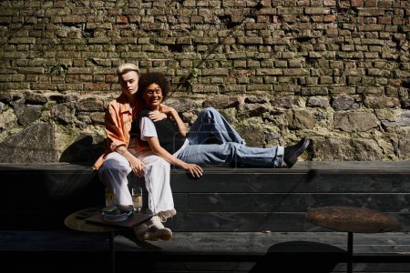A diverse, beautiful lesbian couple sharing a peaceful moment on a rustic wooden bench.