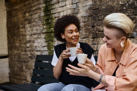 Dos mujeres lesbianas diversas sentadas en un banco, saboreando el café juntas.