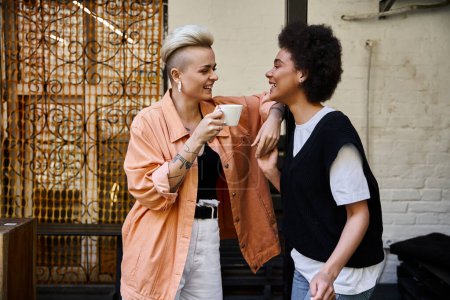 Foto de Una hermosa y diversa pareja de lesbianas de pie una al lado de la otra, en una cita en un café. - Imagen libre de derechos