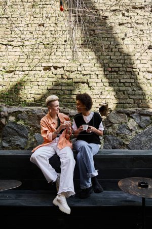 Ein vielfältiges, reizendes lesbisches Paar teilt einen Moment auf einer stilvollen Bank.