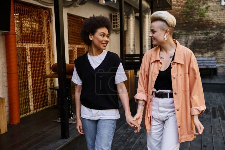 Ein vielfältiges Paar von Lesben teilt einen intimen Moment, als sie Hand in Hand eine Straße hinuntergehen.