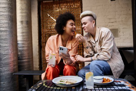 Téléchargez les photos : Un beau couple diversifié de lesbiennes dégustant un repas ensemble dans un café. - en image libre de droit