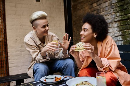 Téléchargez les photos : Deux belles femmes de différentes ethnies s'assoient ensemble à une table, partageant un repas dans un café confortable. - en image libre de droit