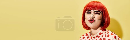 Ein atemberaubender Rotschopf in einem gepunkteten Kleid, das einen kreativen Pop-Art-Make-up-Look vor einem kühnen gelben Hintergrund zeigt.
