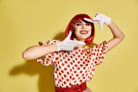 A stylish redhead woman with pop art makeup wearing a polka dot shirt and white gloves on a yellow backdrop.