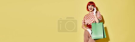 Pretty redhead woman stands holding a green shopping bag in front of a yellow wall, showcasing creative pop art makeup.