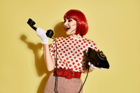 A fiery red-haired woman with striking pop art makeup holds a phone against a yellow background, channeling a comic book character.