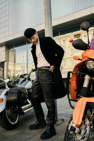 Young red-haired man in debonair attire standing next to a parked motorcycle in the city.