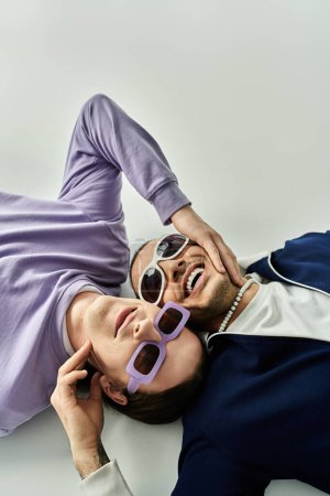 two men laying on the ground, both wearing sunglasses.