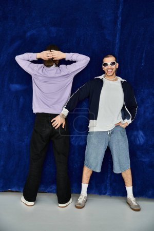 Photo for Two attractive men stand together, posing in front of a vivid blue wall. - Royalty Free Image
