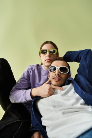 Two men sitting together, both wearing sunglasses.