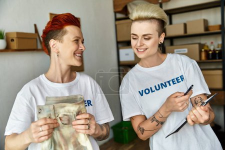 Foto de Dos mujeres, una joven pareja lésbica, se unen en camisetas voluntarias, unidas en obras de caridad. - Imagen libre de derechos