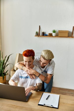 Two women, volunteers in matching shirts, working on a laptop together at a table.