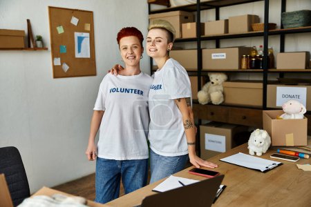 Photo for Two young women, a lesbian couple, wearing volunteer t-shirts, stand side by side in a room, united in charity work. - Royalty Free Image