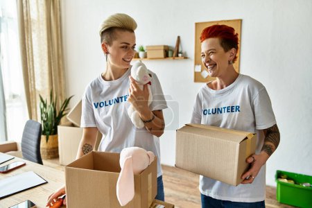 Una joven pareja lesbiana con camisetas voluntarias sosteniendo cajas de donaciones, haciendo trabajo de caridad juntos.