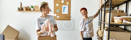 Téléchargez les photos : Un jeune couple de lesbiennes en chemises bénévoles, debout dans une pièce remplie de boîtes, travaillant ensemble pour la charité. - en image libre de droit
