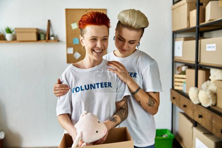 A young man and woman, both wearing volunteer shirts, tenderly hold a toy pig nestled in a box, showing love and care.