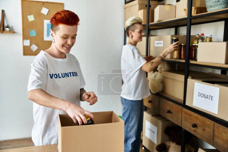 junges lesbisches Paar beim Auspacken von Kartons in einem Raum, während sie sich als Freiwillige engagieren und gemeinnützige Arbeit leisten.