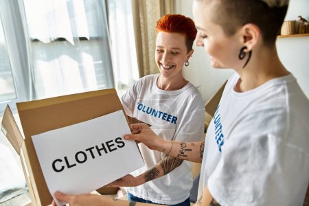 Photo for Two women in volunteer t-shirts standing together with pride and unity as they work on a charity project. - Royalty Free Image